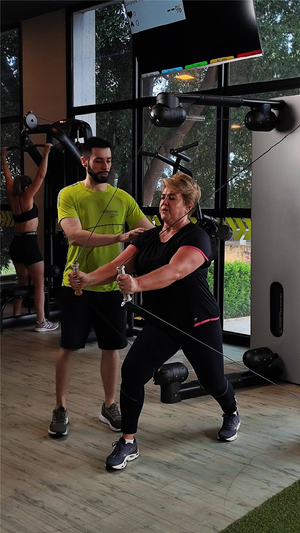 Professor da Corpore Jardim Esplanada acompanha uma aluna durante um exercício com cabos.
